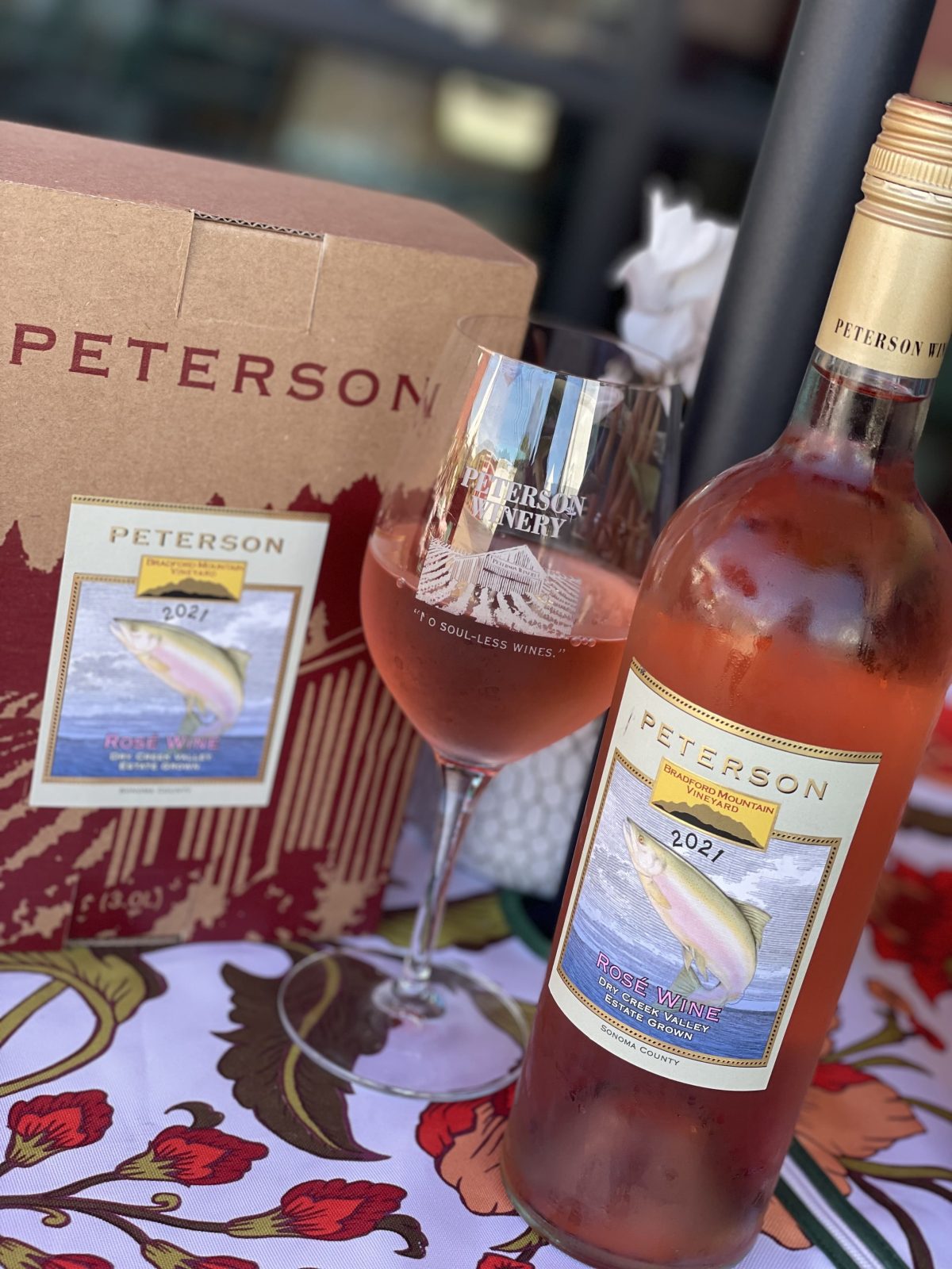 Peterson Winery 2021 Rosé bottle, glass, and branded box on a floral tablecloth.